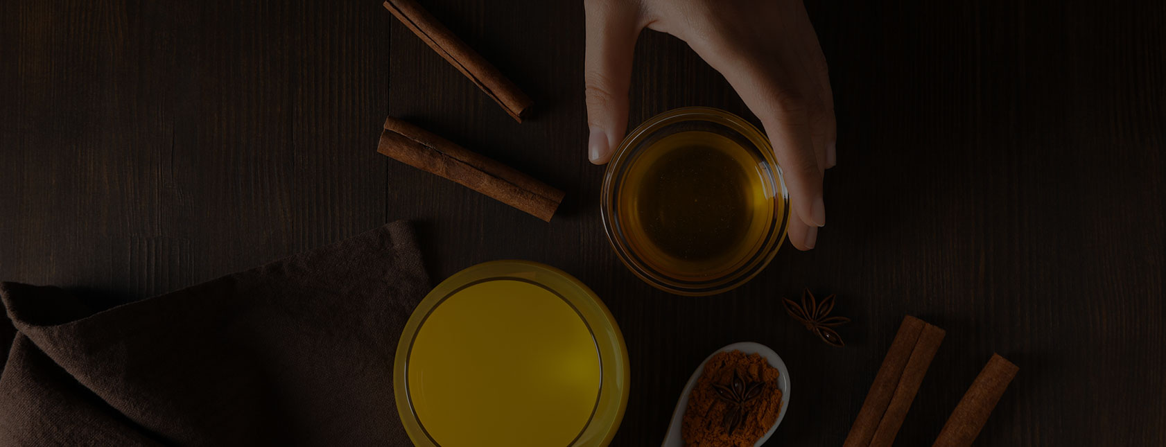 Hand holding honey, spices, cinnamon sticks on wood in banner image on padma home page